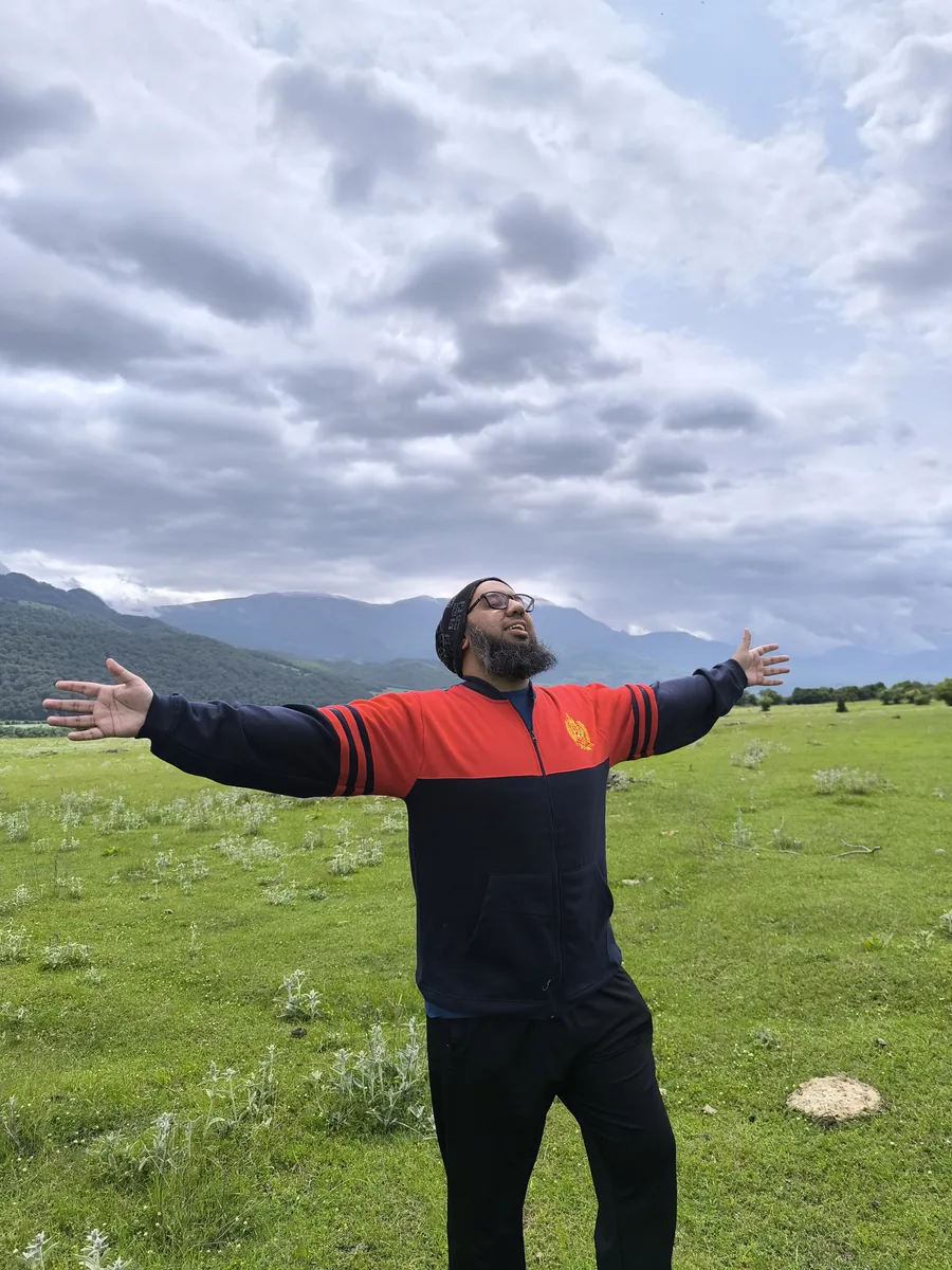 Muhammad Ahsan standing with arms open in a green valley in Azerbaijan